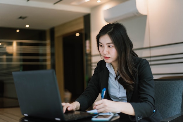 Mooie jonge Aziatische vrouw die haar laptop met behulp van