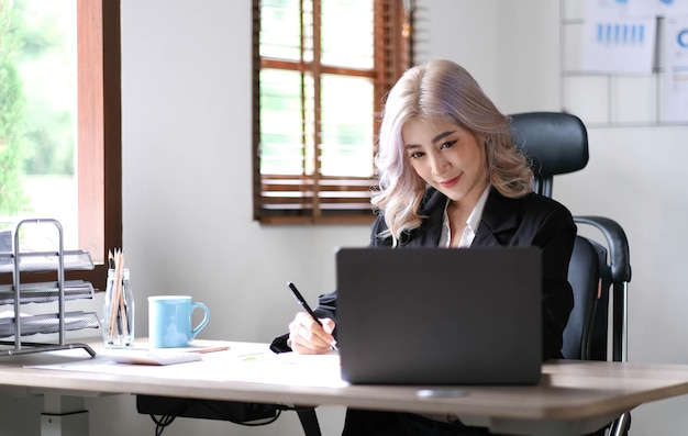 Mooie jonge aziatische vrouw die in een coffeeshop zit met een laptop Gelukkige jonge zakenvrouw die aan tafel zit in een café met een computer met tabbladen