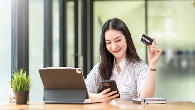 Mooie jonge Aziatische vrouw die smartphone vasthoudt en creditcard gebruikt voor online winkelen