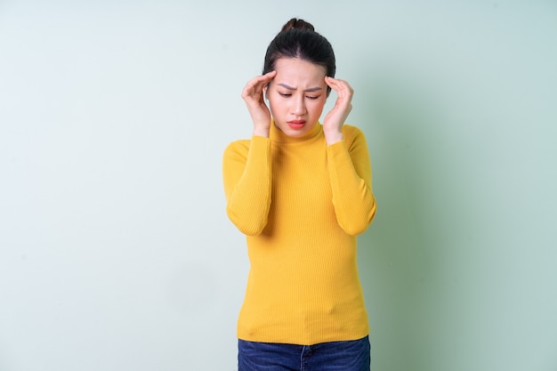 Mooie jonge Aziatische vrouw die sweater op groene achtergrond draagt