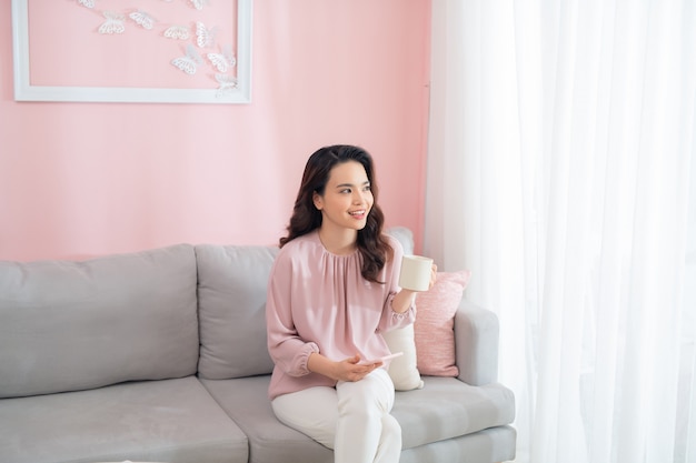 Mooie jonge Aziatische vrouw koffie drinken wanneer het zitten op de bank