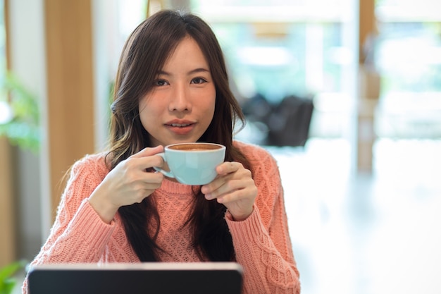 Mooie jonge aziatische vrouw met koffiekop die 's ochtends koffie drinkt in café relax chill