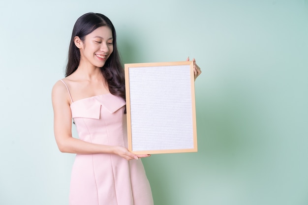 Mooie jonge Aziatische vrouw met wit bord op groene achtergrond