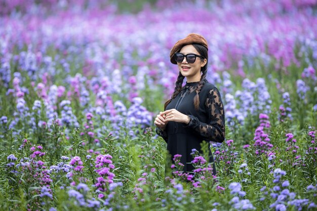 Mooie jonge Aziatische vrouw op zwarte jurk met zwarte zonnebril op violet bloem veld., Aroma concept, Aantrekkelijke jonge Aziatische vrouw buitenshuis aanraken van violette bloemen.