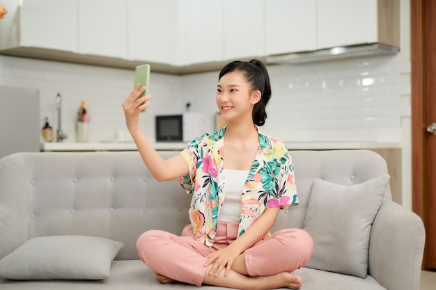 Mooie jonge aziatische vrouw zit op de bank hand met smartphone selfie te nemen