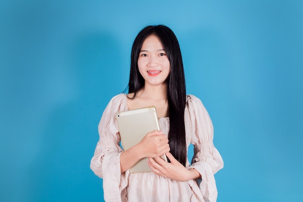 Mooie jonge Aziatische zakenvrouw die digitale tablet vasthoudt terwijl ze op een blauwe achtergrond staat