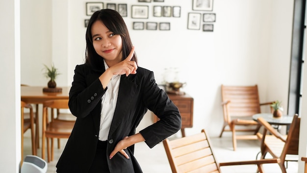 Mooie jonge Aziatische zakenvrouw in pak en wijzende vinger handen omhoog op kantoor