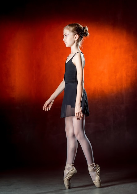 Mooie jonge ballerina danst in de studio op een donkere achtergrond. Een kleine danser. Balletdanser.