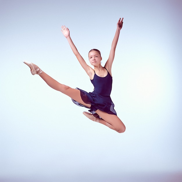 Mooie jonge balletdanser die op een grijze achtergrond springt