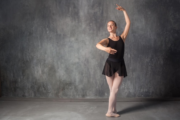 Mooie jonge blonde balletdanser in een zwarte jurk witte panty en bouillant pointes Russisch ballet dansen in een donkere dansstudio