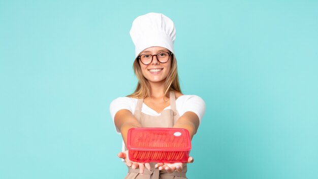 Mooie jonge blonde chef-kokvrouw en houdt een tupperware vast