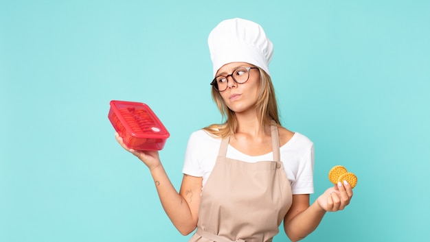 mooie jonge blonde chef-kokvrouw en met een tupperware