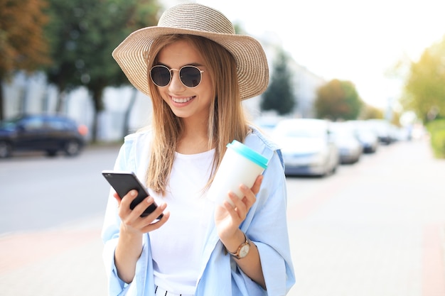 Mooie jonge blonde meid die mobiele telefoon gebruikt terwijl ze buiten staat.