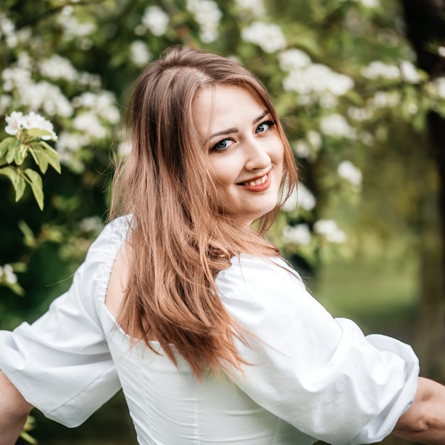 Mooie jonge blonde vrouw die zich dichtbij de appelboom bevindt.