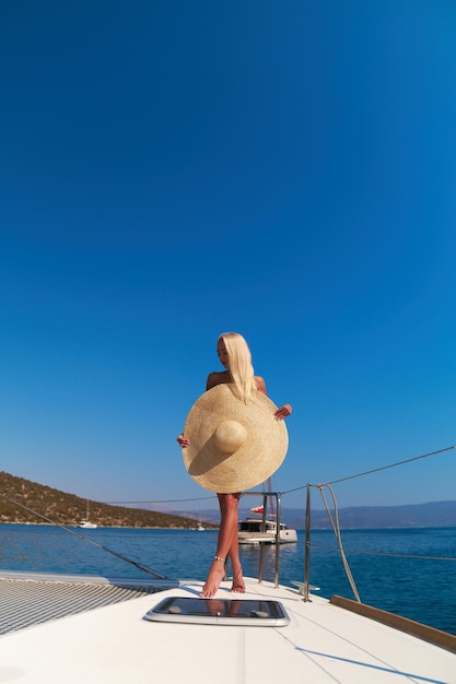 Mooie jonge blonde vrouw in bikini staande op catamaran boog op zonnige zomerdag