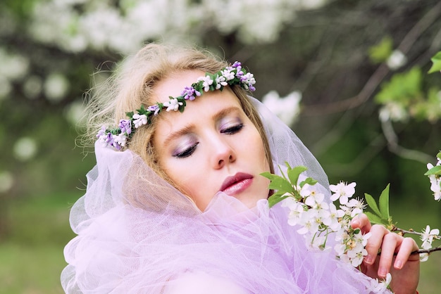 mooie jonge blonde vrouw in bloemenkrans bloeiende bomen in de lente