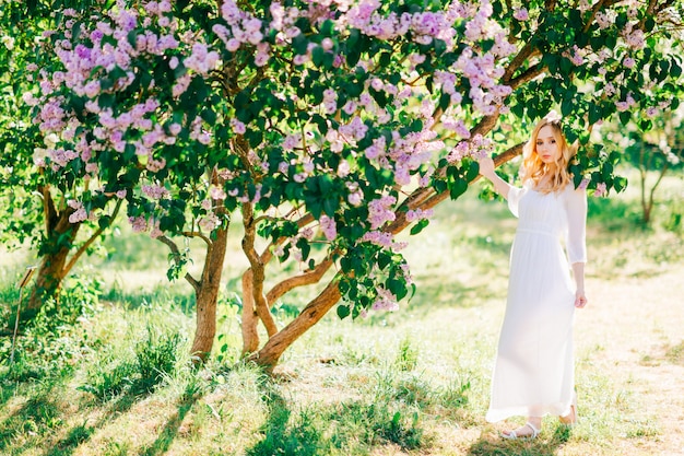 Mooie jonge blonde vrouw in het witte kleding stellen in de zomer zonnig park.