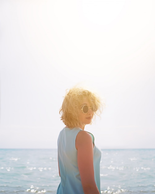 Mooie jonge blonde vrouw in zonnebril op het strand op de achtergrond van een zee