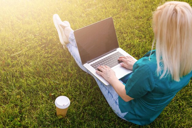 mooie jonge blonde vrouw met een laptop in het park op een warme zomerdag