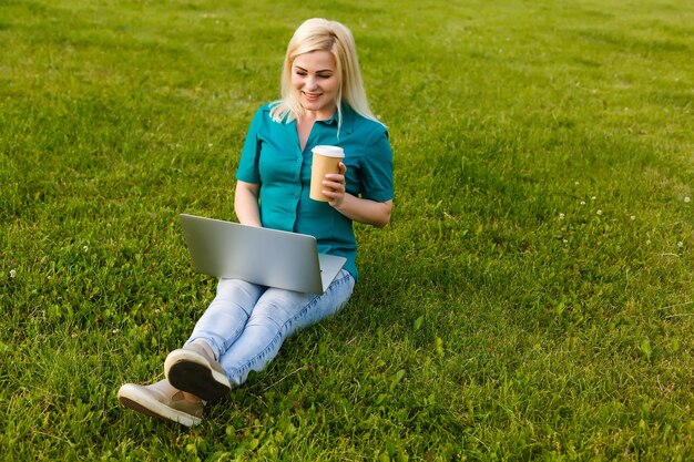 mooie jonge blonde vrouw met een laptop in het park op een warme zomerdag