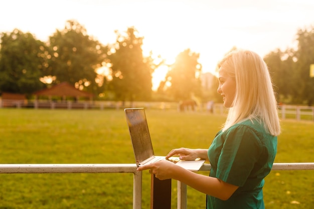 mooie jonge blonde vrouw met een laptop in het park op een warme zomerdag