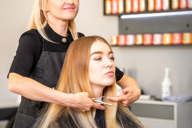 Mooie jonge blonde vrouw met lang steil blond haar dat een kapsel krijgt bij de kapsalon