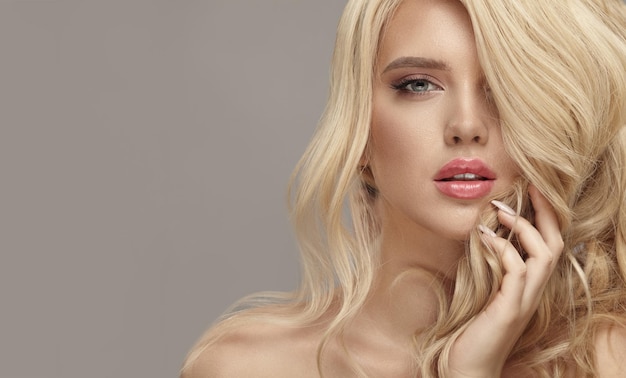 Mooie jonge blonde vrouw met naakte make-up heeft een krullend lang helder haar close-up studioportret