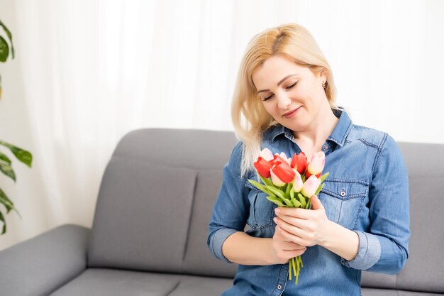 Mooie jonge blonde vrouw met tulpenboeket. Lente portret. Helder roze bloemen in de handen van het meisje. Thuis. Interieur portret.