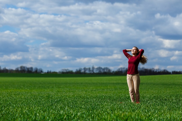 Foto mooie jonge blonde vrouw staat op groen gras in een park. blauwe lucht met wolken. het meisje lacht en geniet van een goede dag.
