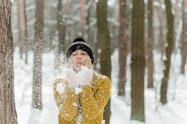 Mooie jonge blonde vrouw, warm gekleed, met een sjaal en wanten. Mooi meisje met plezier in de sneeuw