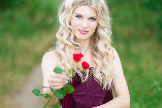 Mooie jonge blondevrouw die met krullend haar een mandhoogtepunt van rode rozen houden. Zachte focus