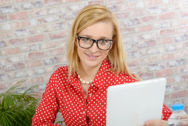 Mooie jonge blondevrouw met rood overhemd die tablet gebruiken