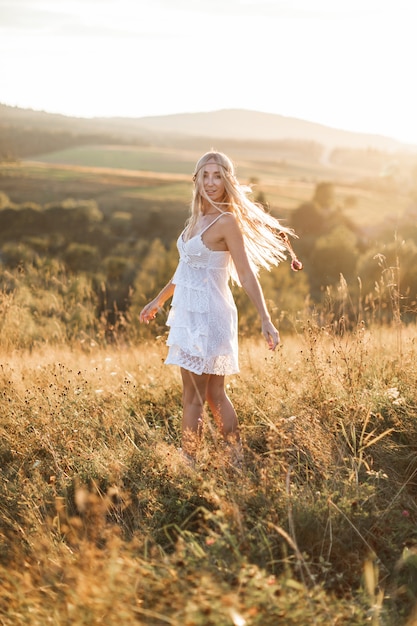 Mooie jonge boho stijl vrouw in witte jurk en met veren in haar lopen op zomer veld