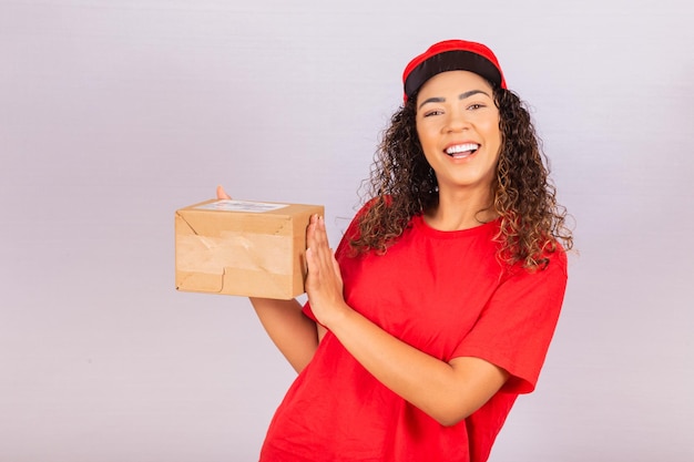 Mooie jonge boodschapper die een pakket levert. Een bezorger in een rood uniform lacht met een pakketje in haar handen. Online winkelen. Gelijkheid van vrouwen.
