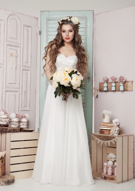 Mooie jonge bruid met kroonbloemen en romantische roze en groene decoratie. Houten kistenflessen en verschillende huwelijksdecoratie
