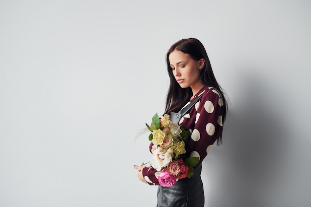 Mooie jonge brunette in zwarte rok die binnenshuis tegen een witte achtergrond staat met een boeket in handen