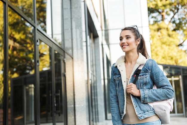 Mooie jonge brunette vrouw jas dragen, dragen rugzak buiten wandelen