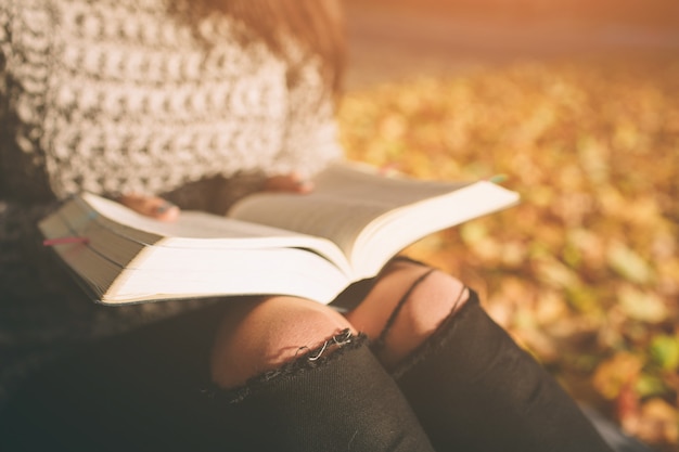 Mooie jonge brunette zittend op gevallen herfstbladeren in een park