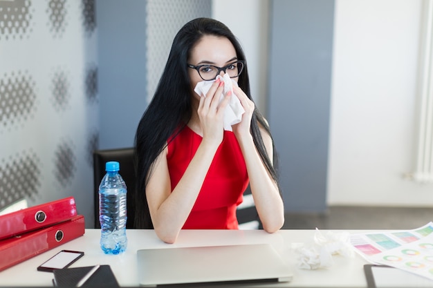 Mooie, jonge businesslady in rode jurk en bril zitten aan de tafel en werken