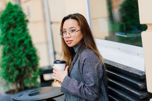 Mooie jonge chinese student met een kopje koffie in de straat