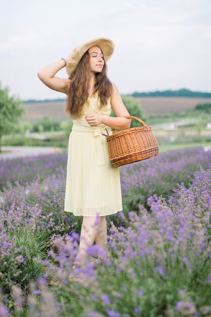 Mooie jonge dame, wandelen met rieten tas in zomerbloeiend lavendelveld