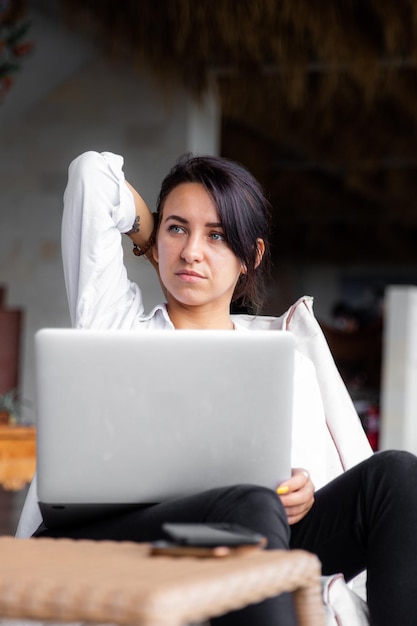 Mooie jonge, diverse vrouw die op afstand werkt met behulp van een computerlaptop die tijd doorbrengt in een stoel in café