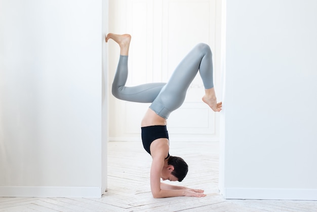 mooie jonge fitnessblogger die een moeilijke handstand doet op een witte achtergrond binnenshuis