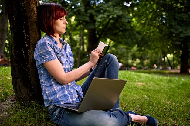 Mooie jonge freelancer vrouw met laptop zitting onder de boom in het park.