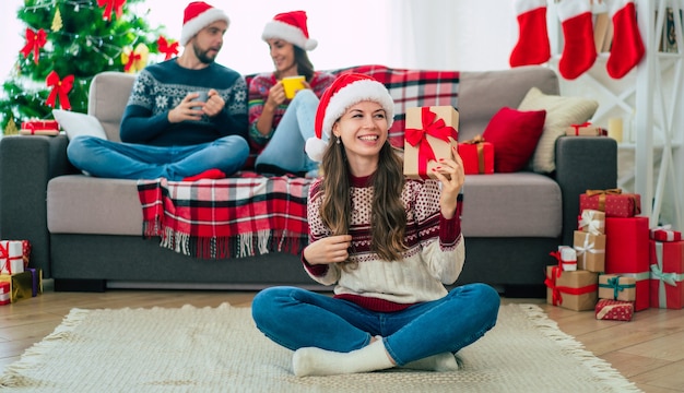 mooie jonge gelukkig lachende vrouw in een kerst trui en kerstmuts houdt een geschenkdoos