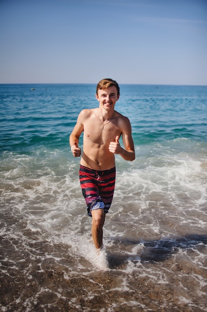 Mooie jonge gelukkig man loopt langs de golven in het water op het strand.