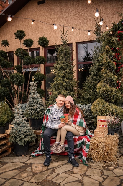 Mooie jonge gelukkige lachende paar gewikkeld in een Schotse deken Groene kerstbomen op de achtergrond De wintervakantie Wachten op het nieuwe jaar