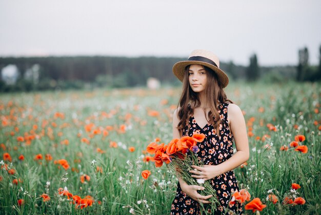 Mooie jonge gratis meisje in een hoed in een zomer veld van rode papavers met een boeket