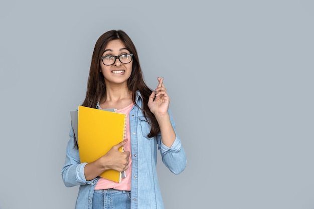 Mooie jonge Indiase vrouw die de vinger kruist op een geïsoleerde grijze achtergrond.