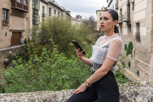 Mooie jonge kaukasische donkerbruine vrouw die smartphone in zwart-witte kleren bekijkt